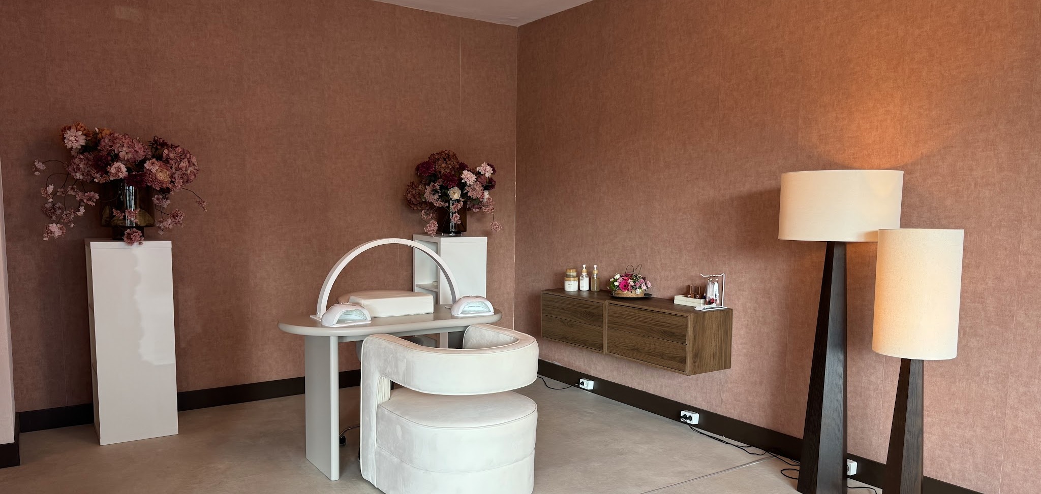 De salon van Noaréa Beauty: roze wanden, witte behandelstoel met gebogen nagellamp en staande lampen